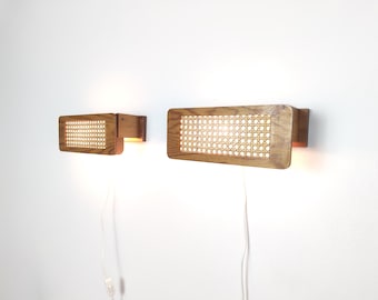 Puede incluir: Dos lámparas de pared rectangulares con marcos de madera de color marrón claro y paneles de rejilla tejida. Cada lámpara emite un brillo cálido a través del patrón de malla e incluye un cable eléctrico blanco con un pequeño interruptor.