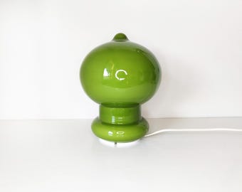 Könnte beinhalten: Grüne Glas-Tischlampe mit rundem Schirm und Sockel. Die Lampe hat eine glänzende Oberfläche und eine kleine, abgerundete Spitze. Ein weißes Netzkabel erstreckt sich vom Sockel.