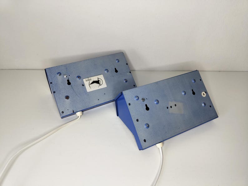 May include: Two blue metal wall sconces with white cords. The sconces have a rectangular shape with a blue front and a light blue back. Each sconce has a sticker with a black and white image of a horse.