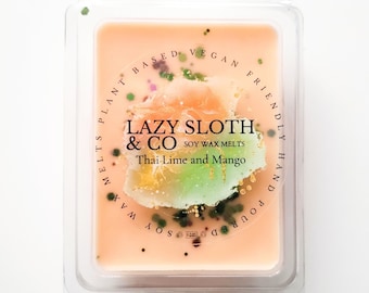 May include: A square soy wax melt in a clear plastic container. The wax melt is a light peach color with a green and gold swirl. The label reads "LAZY SLOTH & CO SOY WAX MELTS Thai Lime and Mango" and is surrounded by the text "MELTS PLANT BASED VEGAN FRIENDLY HAND POURED SOY WAX".