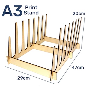 Puede incluir: Soporte de impresión A3 de madera clara, de 29 cm de ancho, 47 cm de largo y 20 cm de alto. Cuenta con divisores verticales. El texto "A3 Print Stand" es visible.