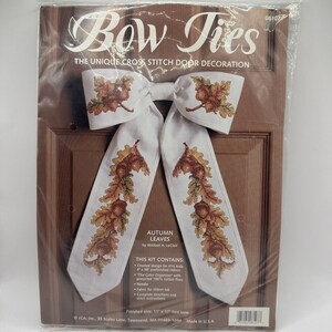 Puede incluir: Un kit de punto de cruz para una decoración de puerta con un lazo blanco con hojas de otoño y bellotas. El kit incluye hilo de algodón pre-ordenado, una aguja, tela para una pestaña de cinta e instrucciones. El tamaño terminado es de 28 cm por 43 cm.