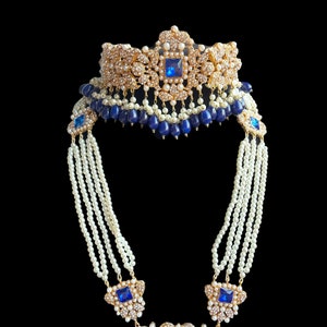 Puede incluir: Un collar de oro y blanco con detalles de piedras preciosas azules. El collar tiene varias hileras de perlas y un gran colgante con una piedra preciosa azul en el centro.
