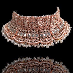 May include: A rose gold choker necklace with white stones and pearls. The necklace is ornate and features a variety of different shapes and sizes of stones.