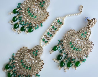 Puede incluir: Un conjunto de joyas dorado ornamentado que incluye un par de pendientes, una diadema y un colgante. Las piezas están adornadas con piedras preciosas transparentes y verde esmeralda, cuentas verdes colgantes y pequeñas perlas blancas. El diseño es intrincado y detallado.
