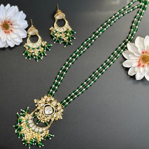 Peut inclure: Un collier de perles vertes et blanches avec un pendentif en or en forme de croissant de lune et des détails complexes. Le pendentif est orné de pierres blanches et de perles vertes. Le collier est assorti à des boucles d'oreilles.