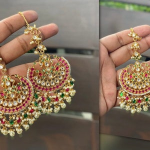 May include: A pair of gold-tone earrings with pink and green gemstones, pearl accents, and a dangling chain.