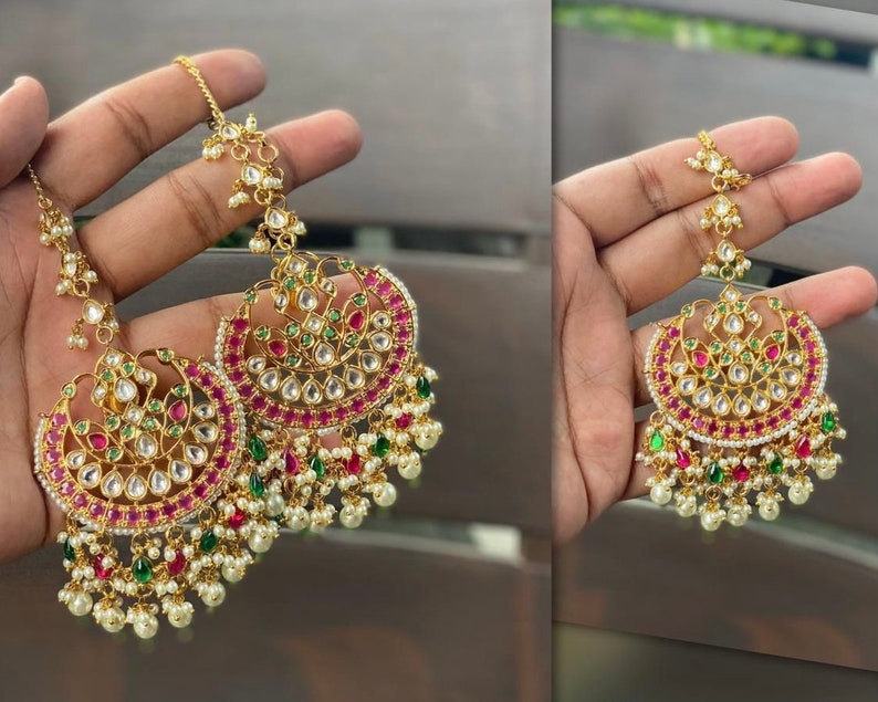 May include: A pair of gold-tone earrings with pink and green gemstones, pearl accents, and a dangling chain.