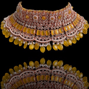 May include: A gold and yellow statement necklace with a large, ornate design. The necklace features a variety of stones, including clear rhinestones and yellow gemstones.