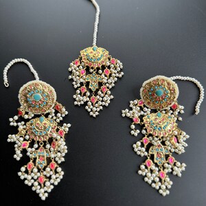 May include: A set of three gold-toned jewellery pieces with pink and turquoise stones. The pieces are adorned with white pearl beads and have a traditional Indian design.