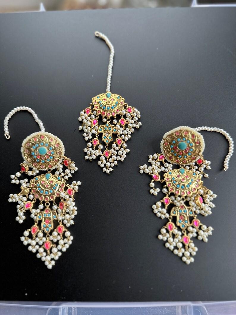 May include: A set of three gold-toned jewellery pieces with pink and turquoise stones. The pieces are adorned with white pearl beads and have a traditional Indian design.