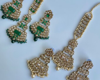 Puede incluir: Un conjunto de dos pares de pendientes y un collar. Los pendientes son de oro con piedras verdes y el collar es de oro con perlas blancas.