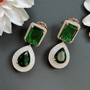 以下が含まれることがあります： エメラルドグリーンの石がクリアなクリスタルハローにセットされた、ドロップタイプのイヤリングのペア。イヤリングはローズゴールド仕上げです。