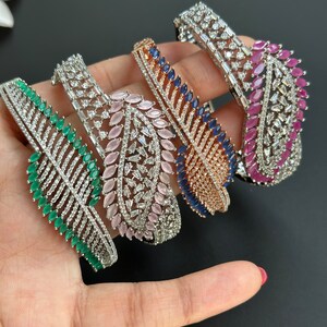 May include: Four silver bracelets with leaf-shaped designs and different colored gemstones. The bracelets feature clear rhinestones and emerald green, pink, blue, and red gemstones.