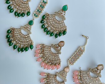 Puede incluir: Un conjunto de tres pares de pendientes con maang tikkas a juego. Los pendientes son de color dorado y presentan un diseño en forma de lágrima con piedras verdes y rosas. Los maang tikkas también son de color dorado y presentan un diseño similar en forma de lágrima.