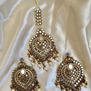 May include: A gold-toned jewelry set with a large, ornate pendant and matching earrings. The pendant and earrings feature a heart-shaped design with mirrored accents and pearl drops.