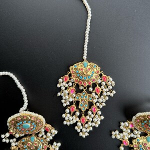 May include: A gold-tone Indian bridal tikka with turquoise and pink stones, pearl drops, and a white pearl chain.