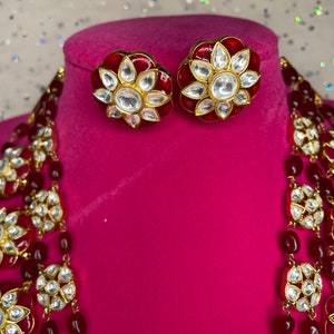 May include: A red and gold necklace with white stones and matching earrings. The necklace has multiple strands of red beads and gold accents.