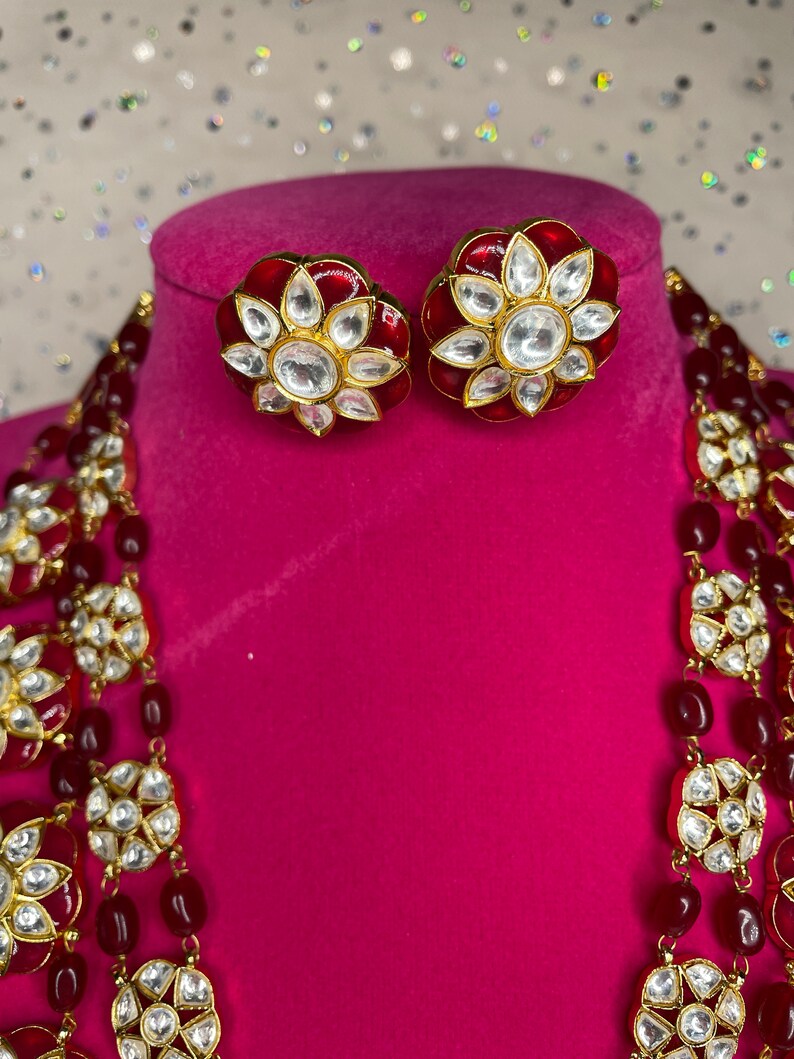 May include: A red and gold necklace with white stones and matching earrings. The necklace has multiple strands of red beads and gold accents.