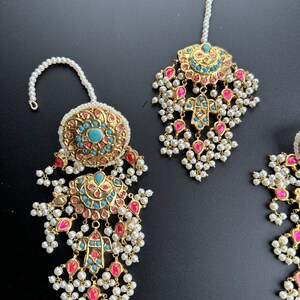 May include: A set of gold-tone jewellery with turquoise and pink stones, pearl accents, and a dangling design. The set includes a maang tikka and earrings.