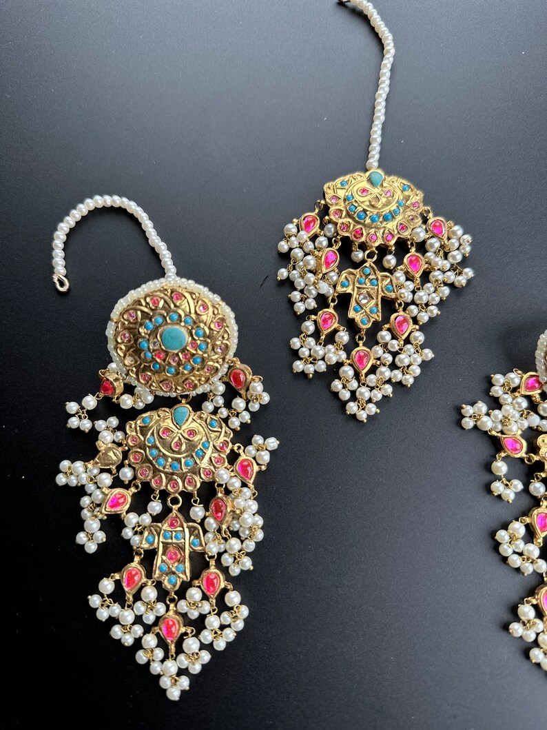 May include: A set of gold-tone jewellery with turquoise and pink stones, pearl accents, and a dangling design. The set includes a maang tikka and earrings.