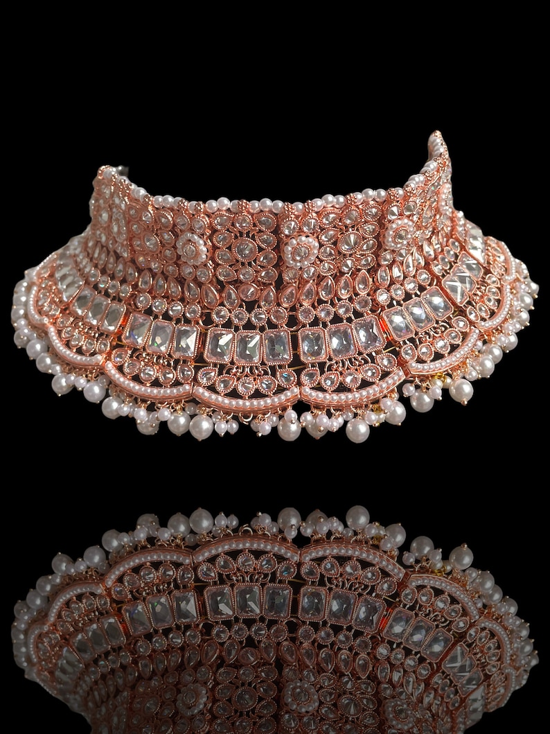 May include: A rose gold choker necklace with white stones and pearls. The necklace is ornate and features a variety of different shapes and sizes of stones.