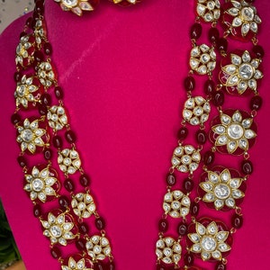 May include: A multi-strand necklace with red beads and gold-toned flower-shaped pendants with white stones. The necklace is paired with matching earrings.