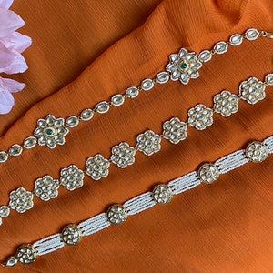 May include: Three gold and white beaded headbands with floral embellishments. The center headband has a green gemstone in the center of the flower.