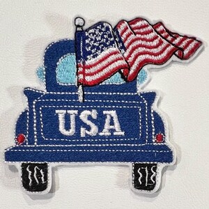 May include: Blue pickup truck with a waving American flag in the back. The truck has the word "USA" written on the back.
