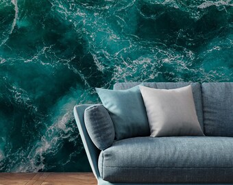 May include: A blue sofa with two pillows sits in front of a wall with a large image of a swirling ocean with white foam.