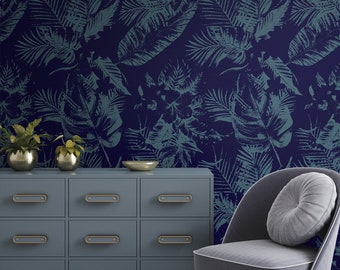 May include: A blue dresser with gold handles and a gray armchair with a gray cushion. The dresser and chair are in front of a wall with a dark blue and teal tropical leaf wallpaper.