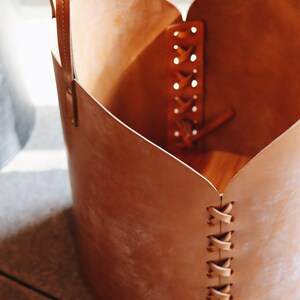 May include: A brown leather basket with a heart-shaped opening and a braided leather strap. The basket has a handle and is made of a natural material.