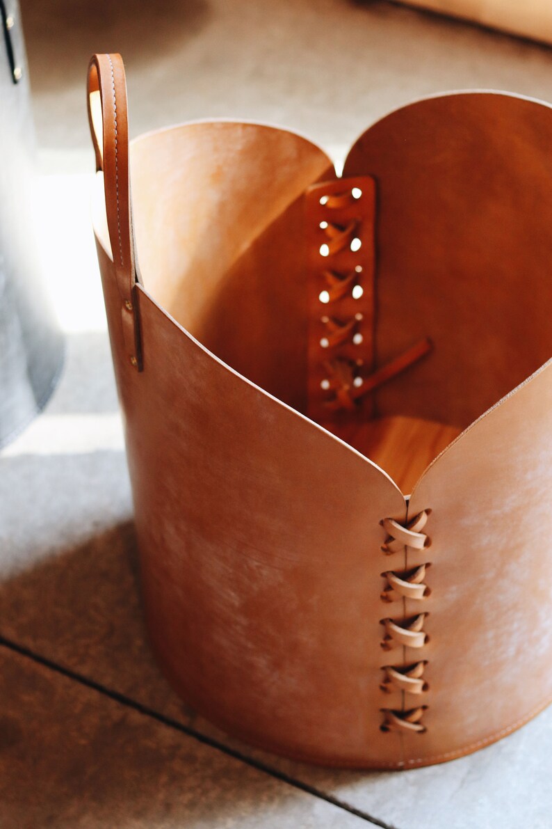 May include: A brown leather basket with a heart-shaped opening and a braided leather strap. The basket has a handle and is made of a natural material.
