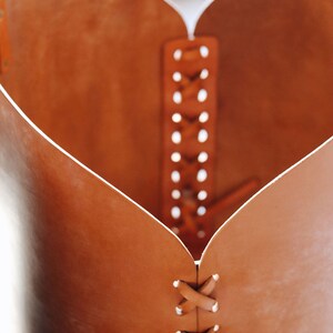 May include: A brown leather heart-shaped container with a braided leather strap detail.