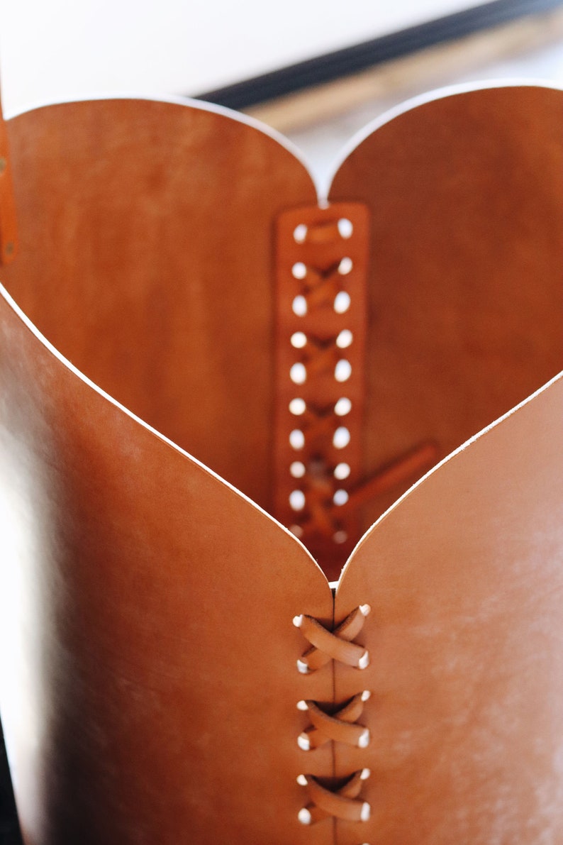 May include: A brown leather heart-shaped container with a braided leather strap detail.