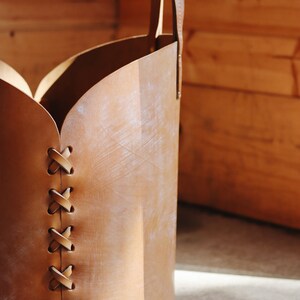 May include: A brown leather storage basket with a handle and a decorative stitched design. The basket is made of natural leather and has a rustic look.