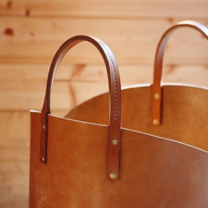 May include: A brown leather tote bag with two handles. The bag is made of a thick, durable leather and has a simple, classic design.