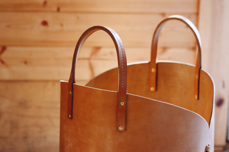 May include: A brown leather tote bag with two handles. The bag is made of a thick, durable leather and has a simple, classic design.