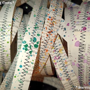 May include: A collection of paper strips with a zig-zag edge, painted with colourful watercolours. The strips are curled and overlapping, creating a layered effect. The text on the strips is mostly illegible, but the words "Starving Emma" appear at the top and bottom of the image.