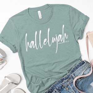 Könnte beinhalten: Ein blaues T-Shirt mit dem Wort "Halleluja" in weißer Kursivschrift. Der Text "PSALM 135:3" ist in kleinerer weißer Schrift unter dem Wort "Halleluja" geschrieben.