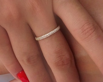 Può includere: Un anello a fascia in oro con piccole pietre trasparenti incastonate attorno all'intera fascia. L'anello è su un dito con smalto rosso. Un gioiello delicato.