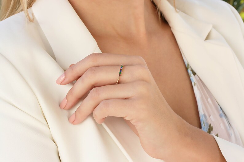 May include: A gold band ring with a row of colorful gemstones. The ring is on a person's finger.