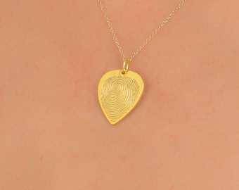 May include: A gold-toned necklace featuring a teardrop-shaped pendant with an engraved fingerprint design. The pendant is suspended from a delicate gold-toned chain, creating a simple and refined piece of jewelry that rests against the skin.