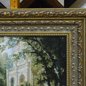 May include: A gold-toned ornate picture frame with a detailed design. The frame surrounds a painting of a white building with trees and a path leading to the building.