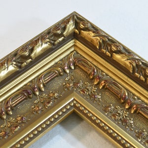 May include: A gold picture frame with ornate detailing and a beaded edge. The frame has a raised, textured design with a floral motif.
