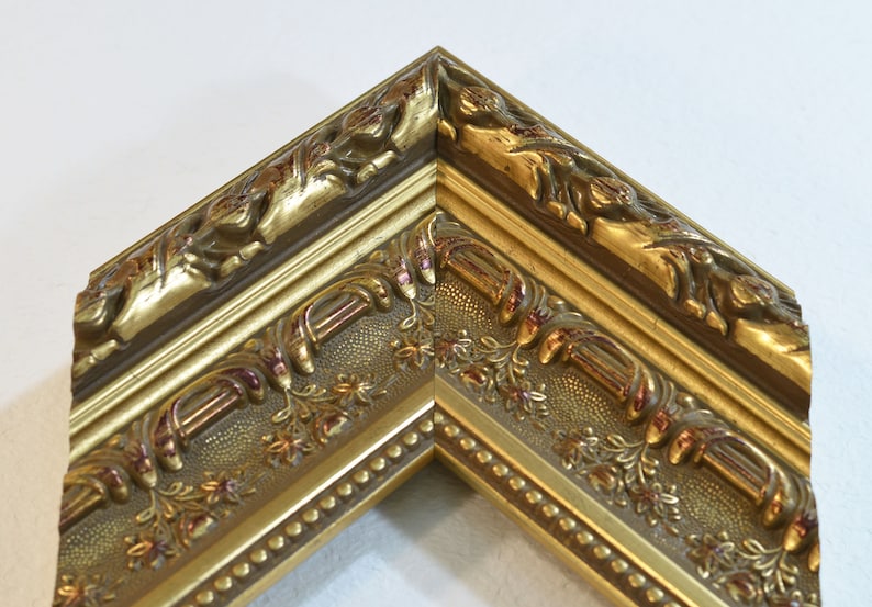 May include: A gold picture frame with ornate detailing and a beaded edge. The frame has a raised, textured design with a floral motif.