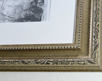 May include: A close-up of a brown picture frame with a decorative floral design. The frame has a beaded edge and a distressed finish.
