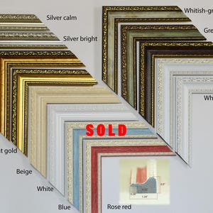May include: A selection of picture frames in various colours and styles, including gold, silver, white, blue, beige, and rose red. The frames are arranged in a fan shape, with the largest frame at the top and the smallest frame at the bottom. The word "SOLD" is written in red letters on the frame in the centre of the image.
