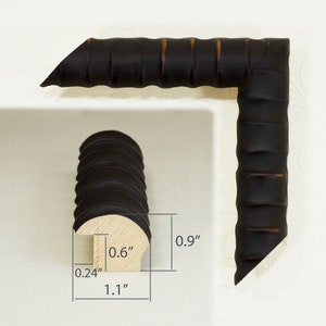 May include: A black picture frame with a ribbed design. The frame is 0.6 inches wide, 0.9 inches tall, and 1.1 inches deep.