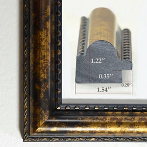 May include: Close-up of a gold picture frame with a black inner edge. The frame has a decorative rope design and a row of small gold beads. The frame is 1.22 inches wide, 0.35 inches deep, and 1.54 inches tall.